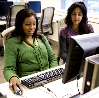 A photo of two women working at a desktop computer.